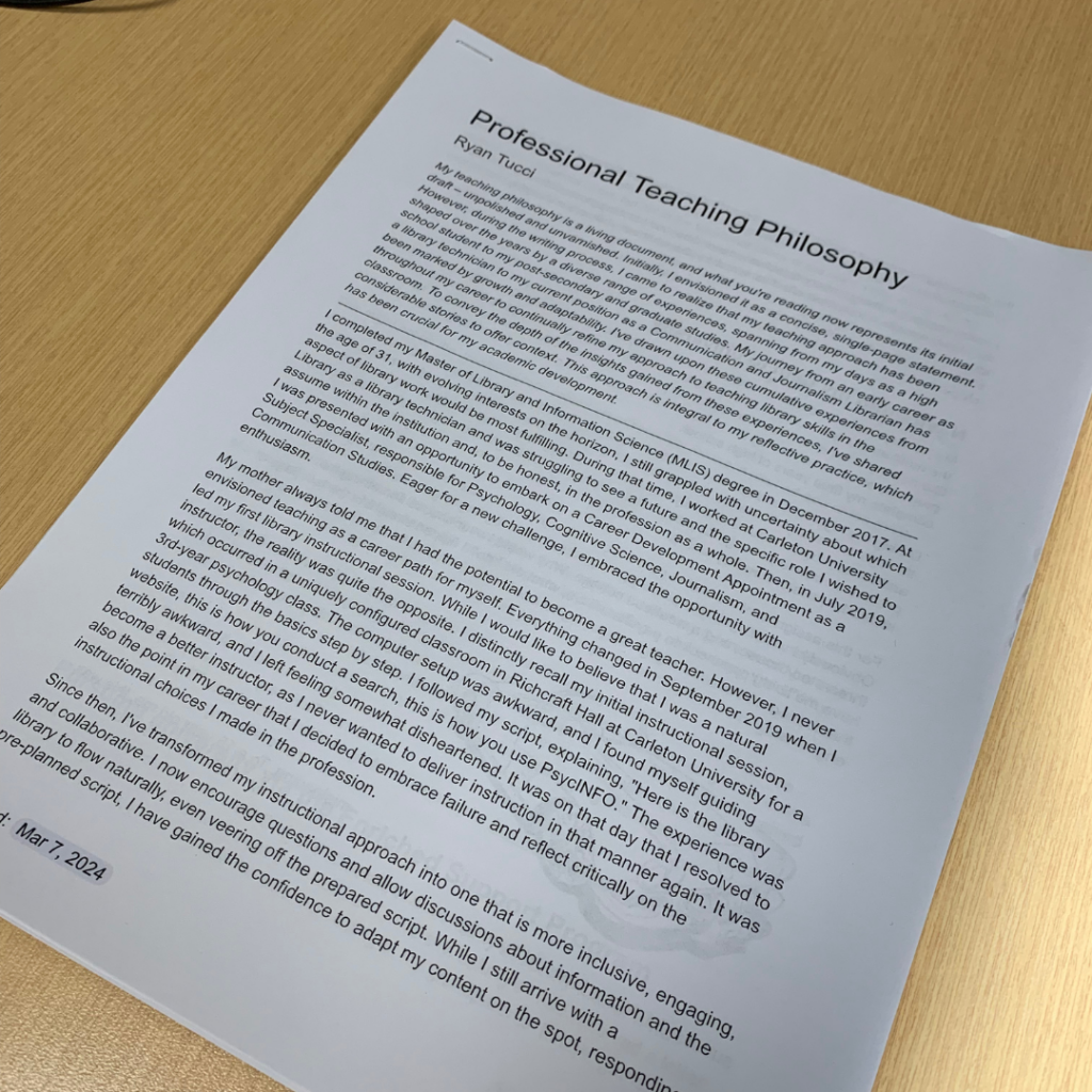 A printed document titled 'Professional Teaching Philosophy' rests on a wooden desk. The text is partially visible and discusses personal experiences and beliefs related to teaching. It mentions completing a Master of Library and Information Science (MLIS) degree, working at a university, and embracing new challenges. A date, 'Mar 7, 2024,' is visible at the bottom, suggesting a recent update or creation of the document. This was a substantial piece of writing I completed earlier this year.